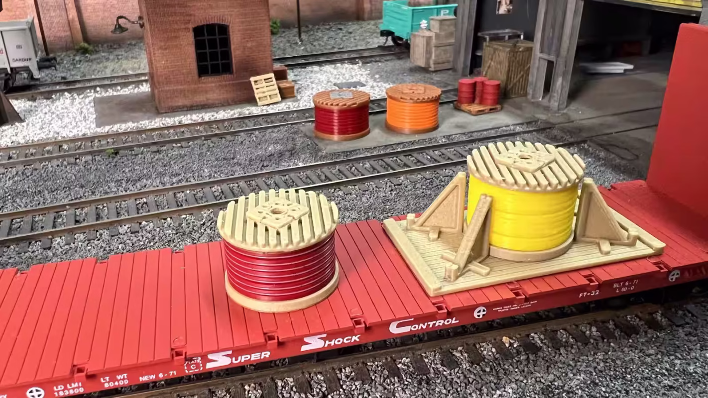 HO scale photo of an angled view of a red and yellow cable drum load on a freight car in a rail yard setting