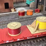 HO scale photo of an angled view of a red and yellow cable drum load on a freight car in a rail yard setting