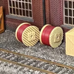 Side view of cable drum load featuring red cables, displayed in a rail yard setting. HO scale