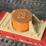 Top view of a HO scale cable drum load featuring an orange drum in the center on a flatbed car set in a rail-yard