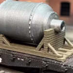 Top view of a winch motor on a flatbed train car in HO scale, emphasizing the silver cylinder, in a rail yard setting.